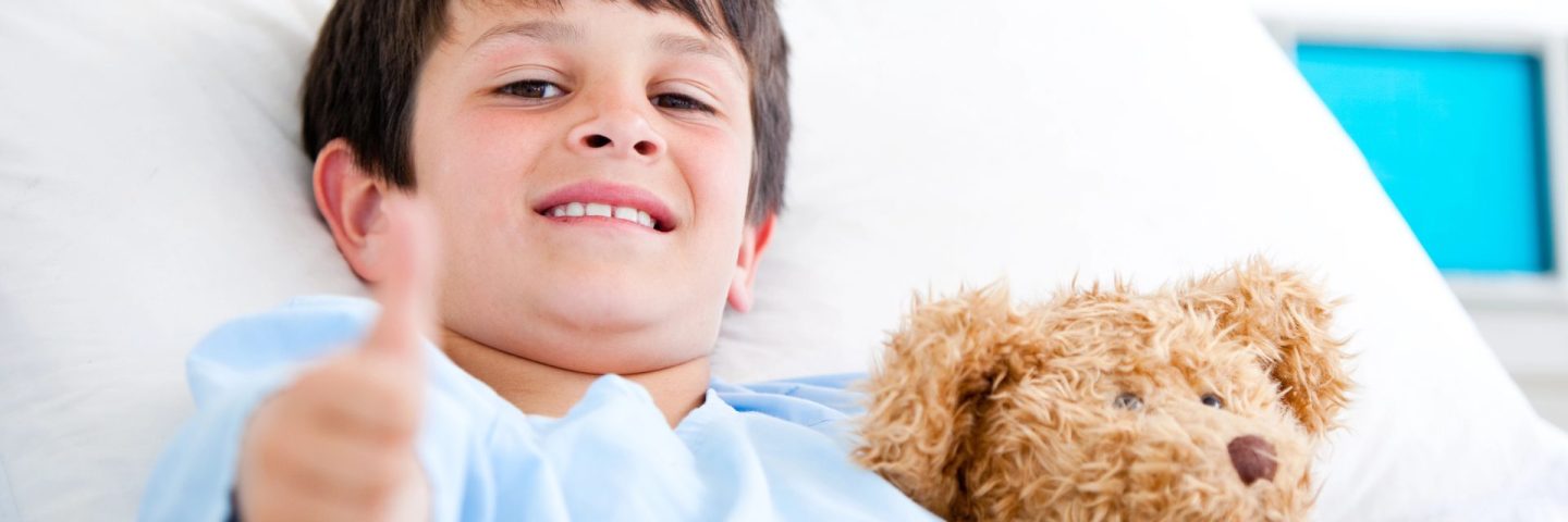 Little boy hugging a teddy bear lying in a hospital bed