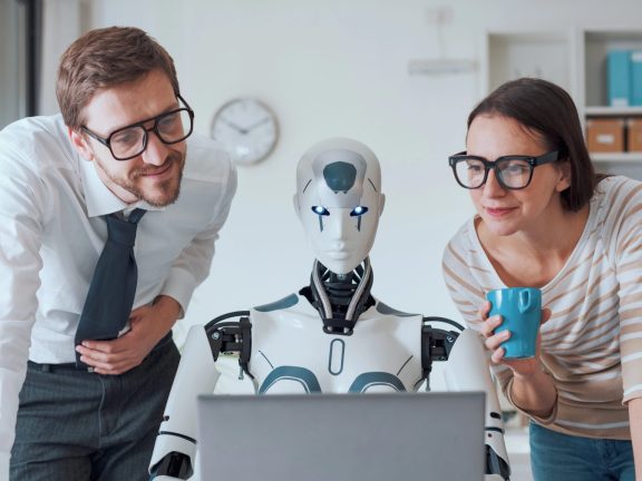 Happy business people supervising an AI robot working in the office