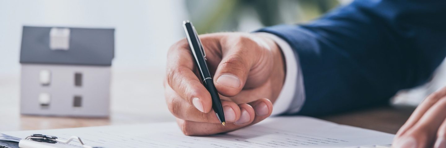 cropped view of businessman using calculator and writing in contract near house model