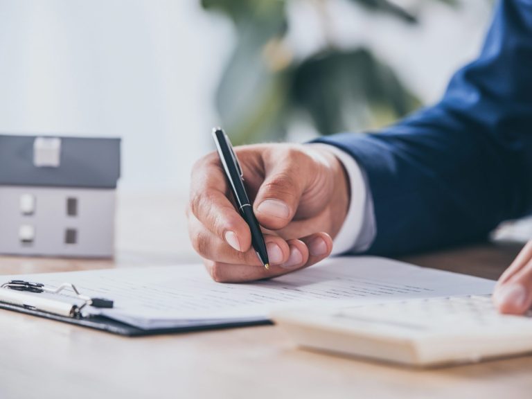cropped view of businessman using calculator and writing in contract near house model