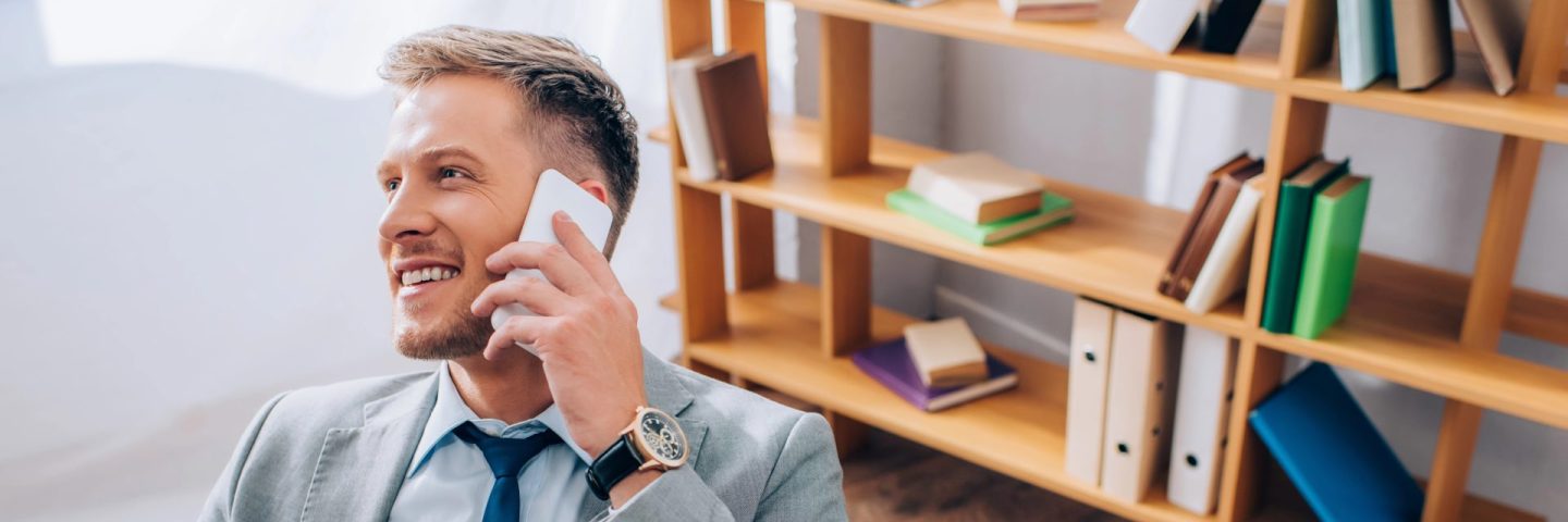 Young businessman in suit smiling while talking on smartphone in office