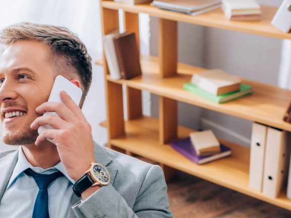 Young businessman in suit smiling while talking on smartphone in office