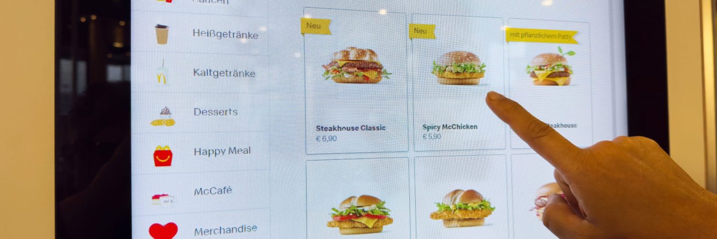 Touchscreen fast food menu display showing burger selection and prices.