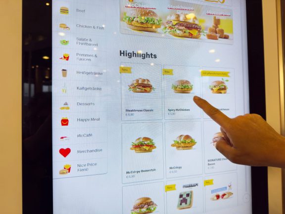 Touchscreen fast food menu display showing burger selection and prices.