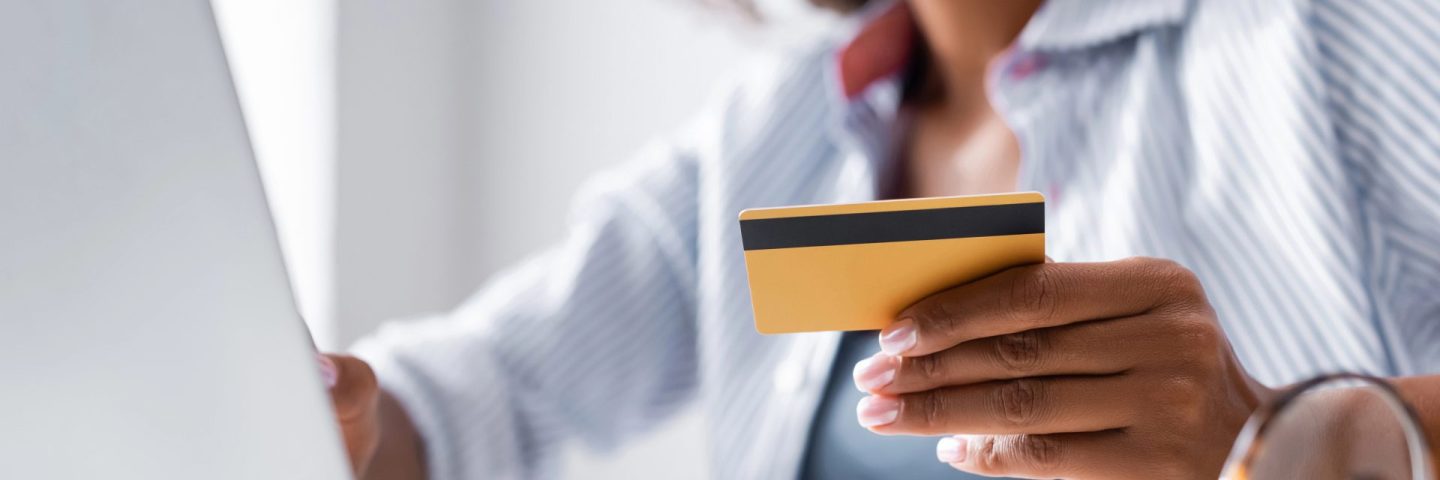 Cropped view of credit card in hand of african american freelancer using laptop near eyeglasses on blurred foreground