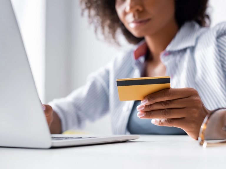 Cropped view of credit card in hand of african american freelancer using laptop near eyeglasses on blurred foreground