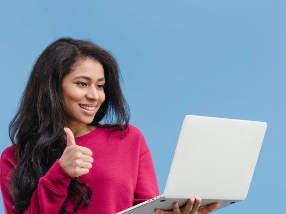 african american woman doing thumb up gesture and holding laptop isolated on blue background