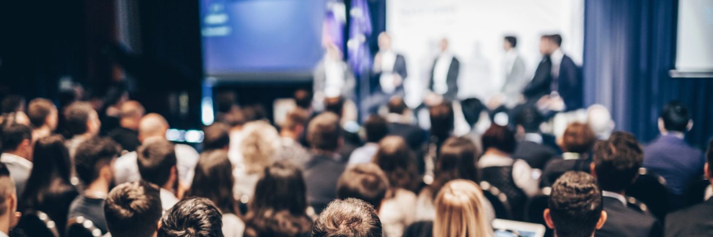 Speaker giving a talk in conference hall at business event. Rear view of unrecognizable people in audience at the conference hall. Business and entrepreneurship concept