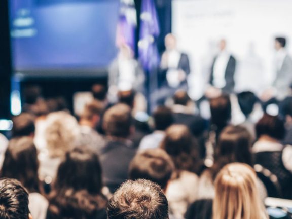 Speaker giving a talk in conference hall at business event. Rear view of unrecognizable people in audience at the conference hall. Business and entrepreneurship concept