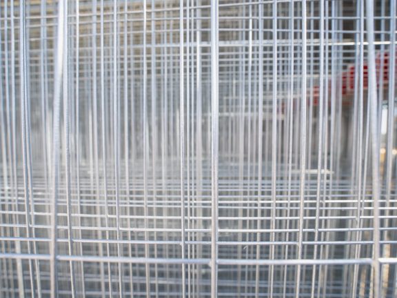 Modular galvanized steel wire grid fencing stored in industrial yard, illustrating equipment inventory, property barrier, and site safety