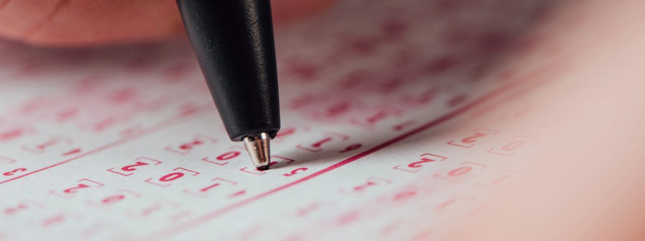 selective focus of hand of gambler marking numbers in lottery ticket with pen