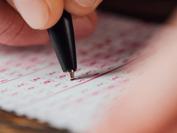 selective focus of hand of gambler marking numbers in lottery ticket with pen